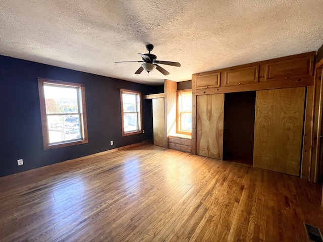 unfurnished bedroom featuring ceiling fan, hardwood / wood-style floors, a textured ceiling, and two closets