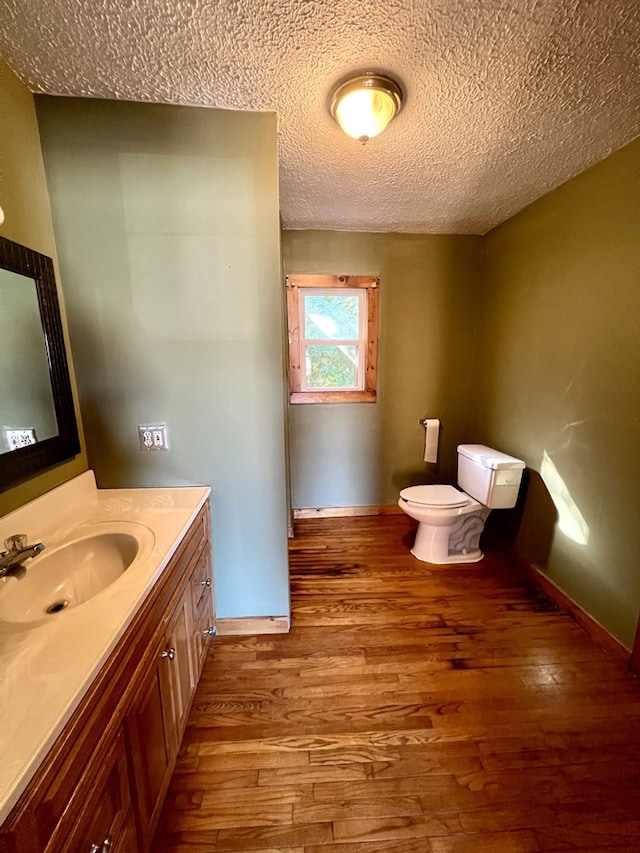 bathroom with wood-type flooring, toilet, vanity, and a textured ceiling