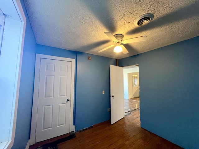 unfurnished bedroom with dark wood-type flooring, ceiling fan, and a textured ceiling