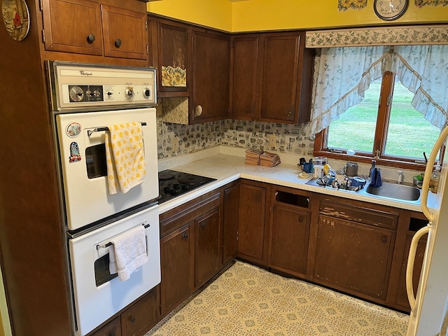 kitchen featuring black electric stovetop, dark brown cabinetry, sink, white double oven, and backsplash