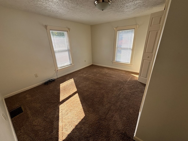 empty room featuring a textured ceiling and dark colored carpet