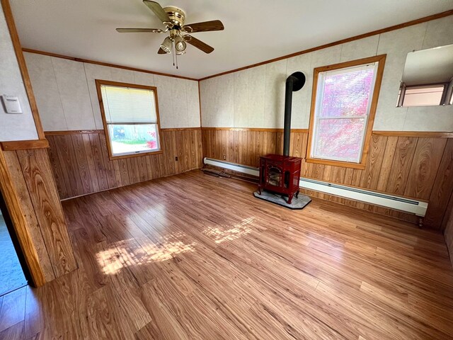 spare room featuring light wood-type flooring, a baseboard radiator, a wood stove, and ceiling fan