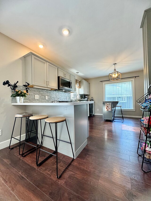 kitchen featuring dark wood-type flooring, gray cabinetry, tasteful backsplash, and a breakfast bar