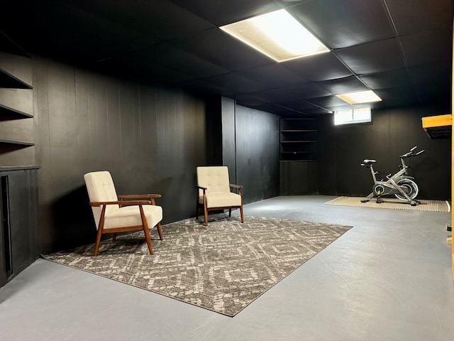 sitting room with concrete flooring, a paneled ceiling, and wood walls