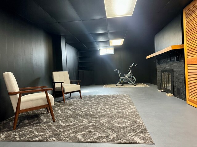 sitting room featuring a brick fireplace, concrete flooring, and wood walls