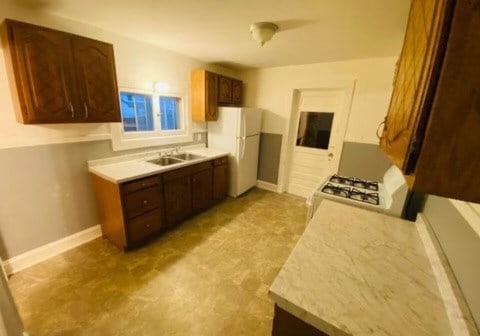 kitchen featuring dark brown cabinetry, range, sink, and white fridge