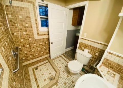 bathroom with tiled shower, toilet, tile patterned flooring, and tile walls