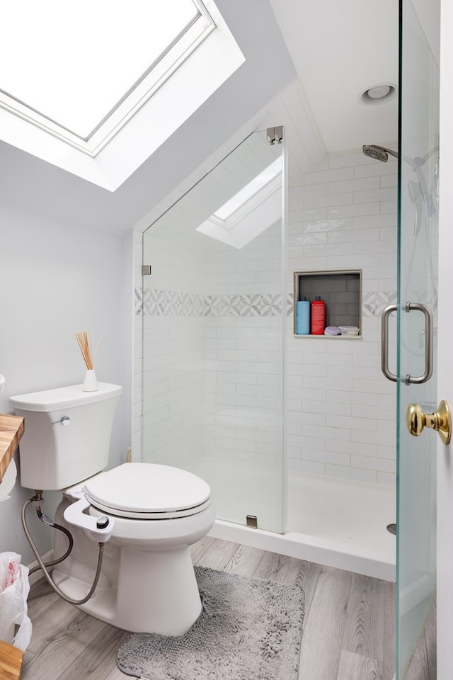 bathroom featuring wood-type flooring, toilet, a shower with shower door, and vaulted ceiling with skylight