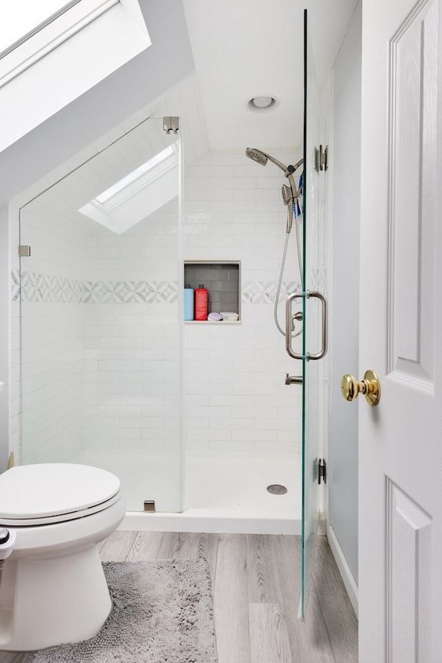 bathroom featuring lofted ceiling, hardwood / wood-style flooring, toilet, and a shower with shower door