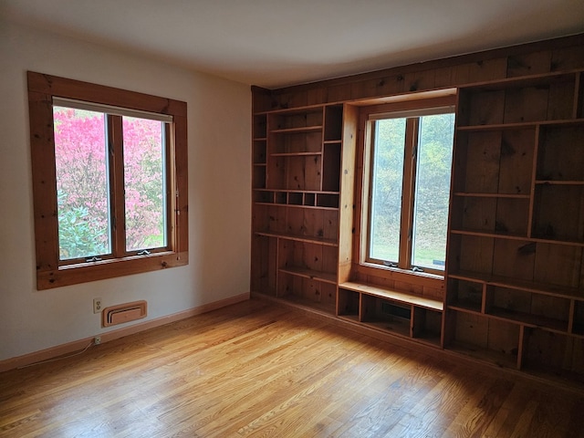 spare room featuring built in features, a wealth of natural light, and light hardwood / wood-style flooring