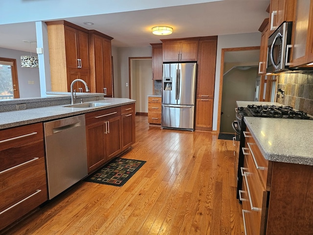 kitchen with appliances with stainless steel finishes, tasteful backsplash, light hardwood / wood-style floors, sink, and light stone counters