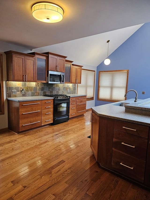 kitchen featuring pendant lighting, vaulted ceiling, black range with gas stovetop, sink, and decorative backsplash