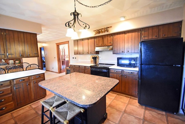 kitchen with light tile patterned flooring, decorative light fixtures, a breakfast bar area, a center island, and black appliances