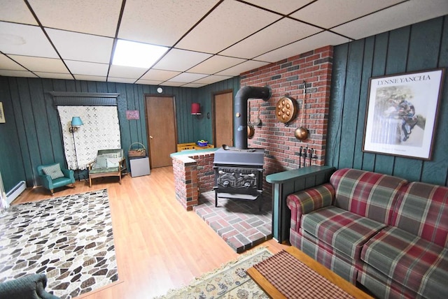 living room with a paneled ceiling, light hardwood / wood-style floors, a wood stove, and a baseboard heating unit