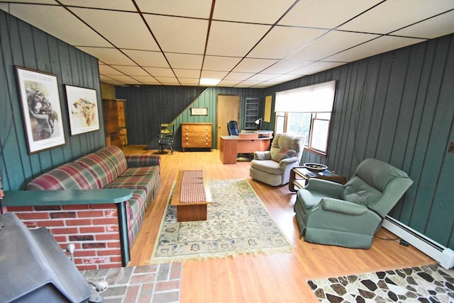 living room with wood walls, wood-type flooring, a drop ceiling, and a baseboard heating unit