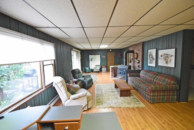 living room with hardwood / wood-style flooring, a wood stove, a drop ceiling, and baseboard heating