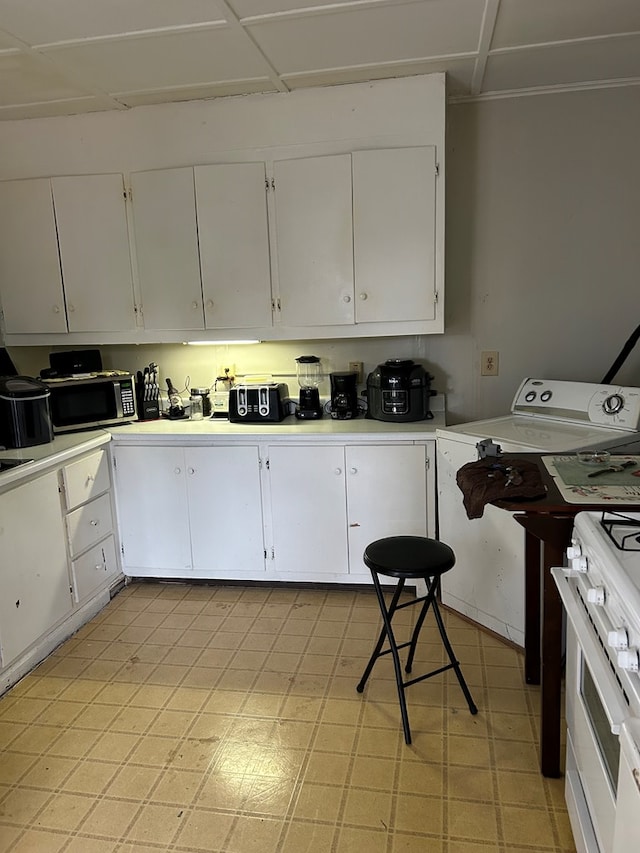 kitchen featuring white stove, white cabinetry, and washer / dryer