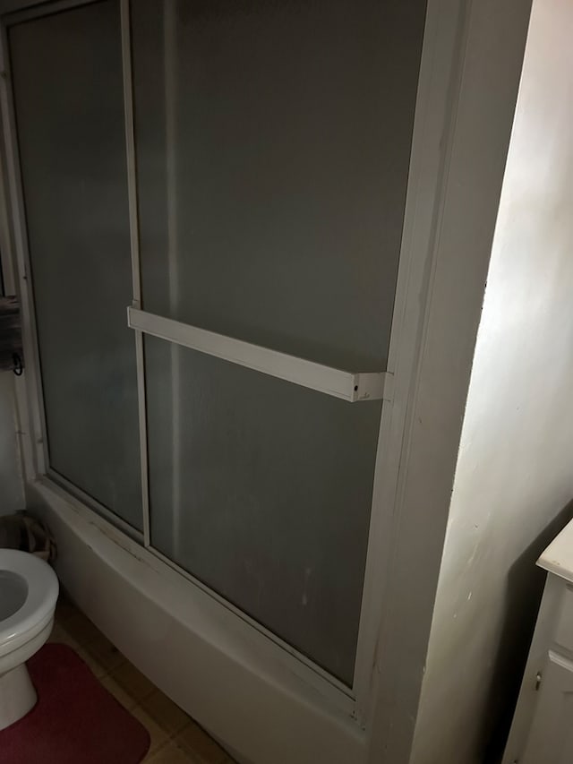 bathroom featuring tile patterned flooring, combined bath / shower with glass door, and toilet