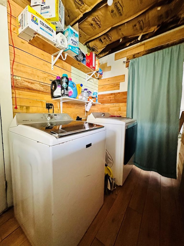 laundry room with wood-type flooring, wooden walls, and washing machine and clothes dryer