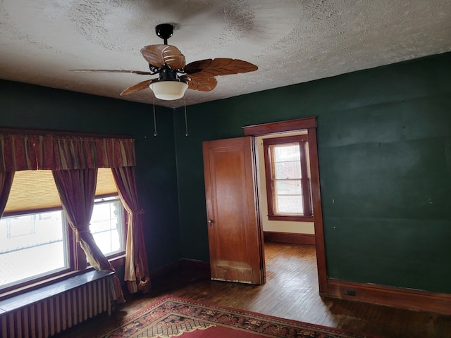 unfurnished bedroom with a textured ceiling, dark wood-type flooring, radiator, and ceiling fan