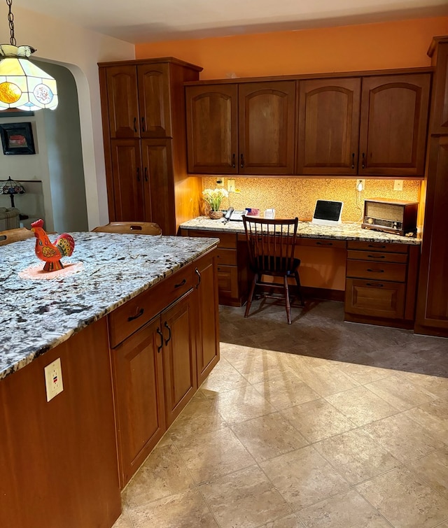 kitchen with built in desk, decorative light fixtures, and light stone countertops