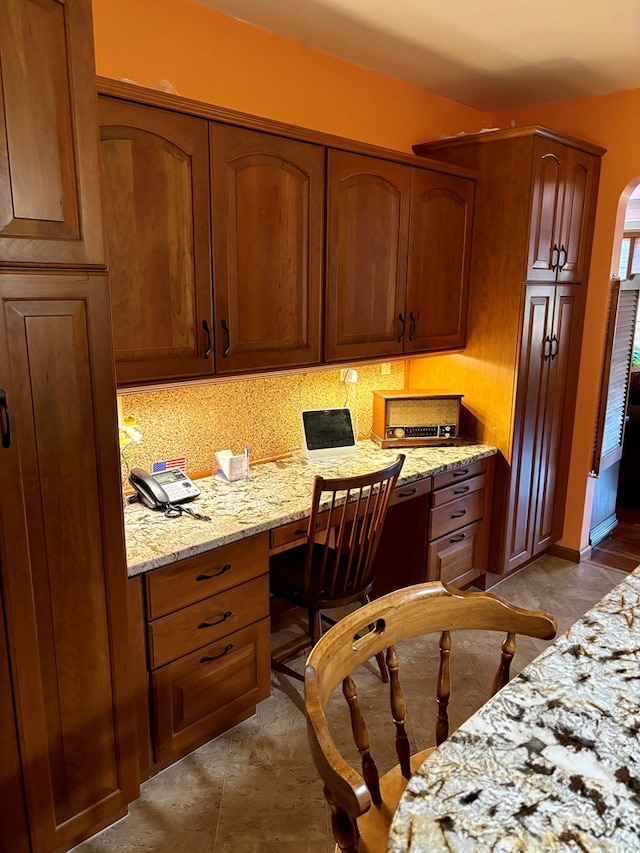 kitchen featuring built in desk, backsplash, and light stone counters