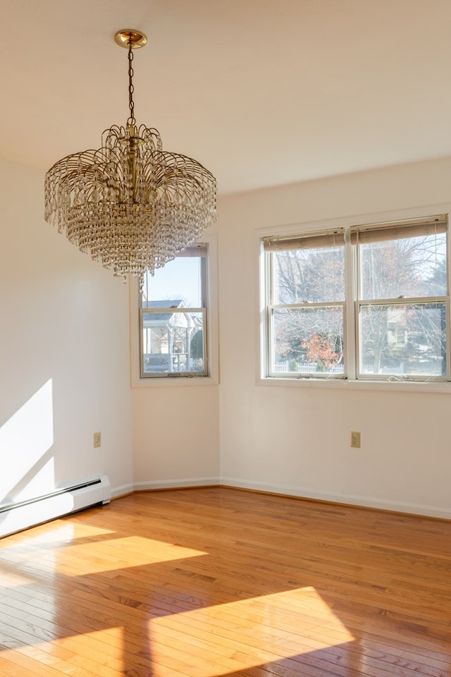 spare room with a baseboard radiator, light wood-type flooring, and an inviting chandelier