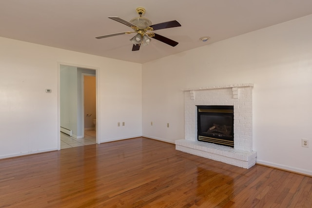 unfurnished living room with a baseboard heating unit, a fireplace, ceiling fan, and light hardwood / wood-style floors