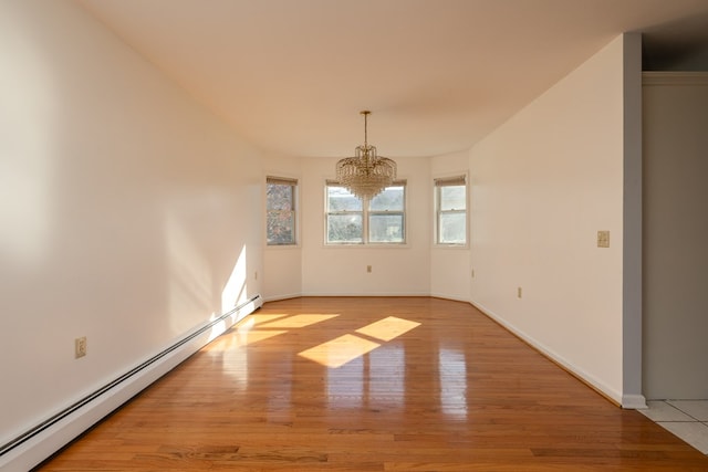 spare room featuring a notable chandelier, light wood-type flooring, and a baseboard heating unit