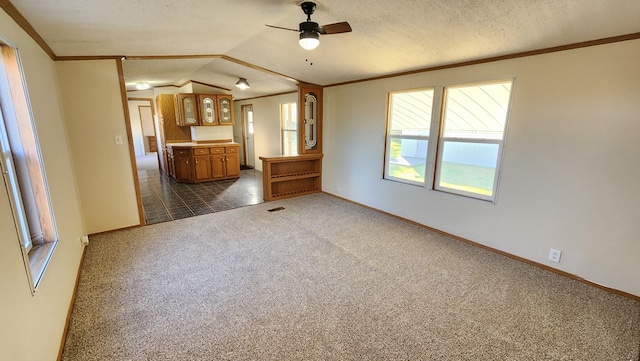 unfurnished living room featuring ceiling fan, a textured ceiling, lofted ceiling, dark carpet, and ornamental molding