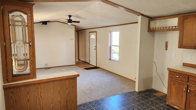 carpeted entryway featuring a textured ceiling, vaulted ceiling, ceiling fan, and ornamental molding