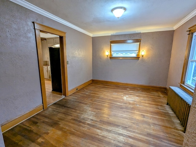 empty room with hardwood / wood-style flooring, ornamental molding, radiator, and a textured ceiling