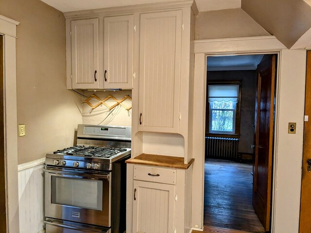 kitchen with stainless steel gas range oven, crown molding, white cabinets, hardwood / wood-style floors, and radiator heating unit