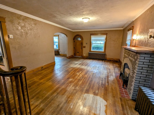 unfurnished living room featuring radiator heating unit, wood-type flooring, crown molding, a brick fireplace, and a textured ceiling