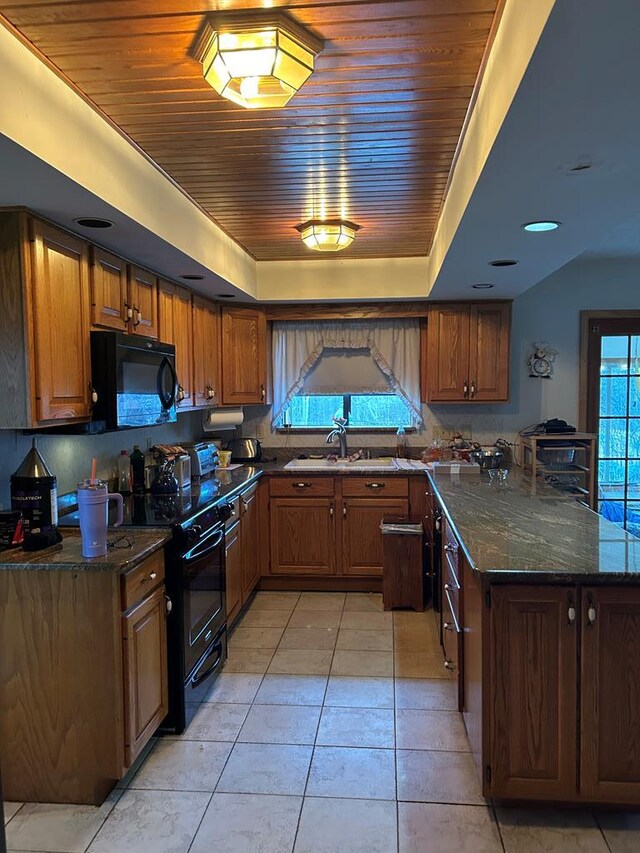 kitchen featuring dark stone counters, black appliances, a raised ceiling, sink, and light tile patterned floors