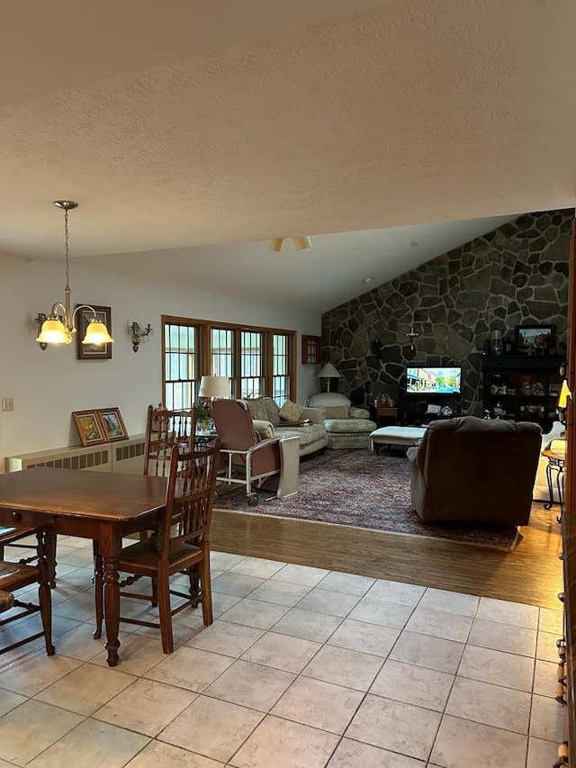 tiled dining room featuring a textured ceiling, vaulted ceiling, an inviting chandelier, and a stone fireplace