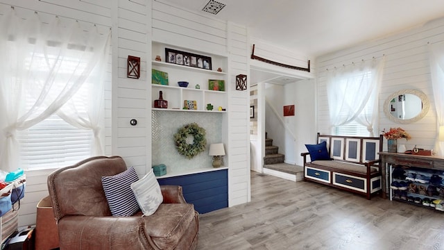 living area featuring built in shelves, a wealth of natural light, wood-type flooring, and wood walls