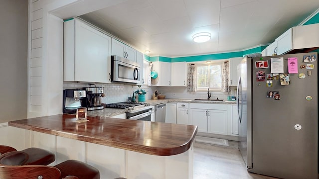 kitchen featuring kitchen peninsula, appliances with stainless steel finishes, sink, white cabinets, and a breakfast bar area