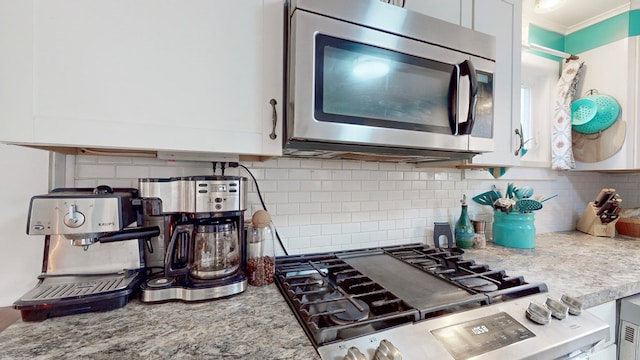 kitchen featuring stove, backsplash, white cabinetry, and light stone counters