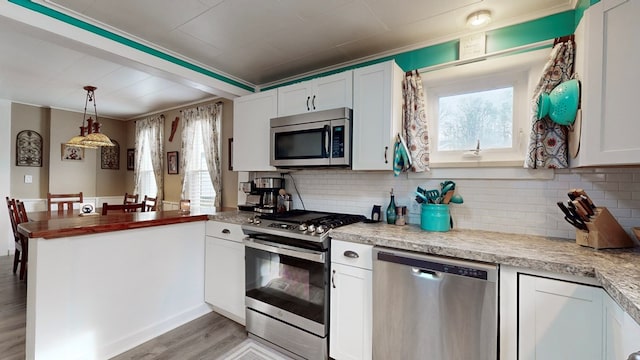 kitchen with backsplash, hanging light fixtures, white cabinets, and stainless steel appliances