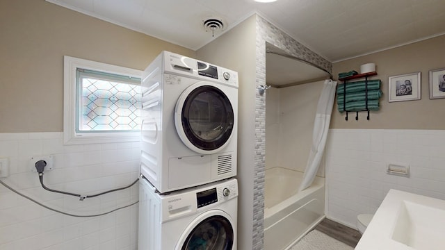 laundry room featuring wood-type flooring, stacked washing maching and dryer, tile walls, and ornamental molding