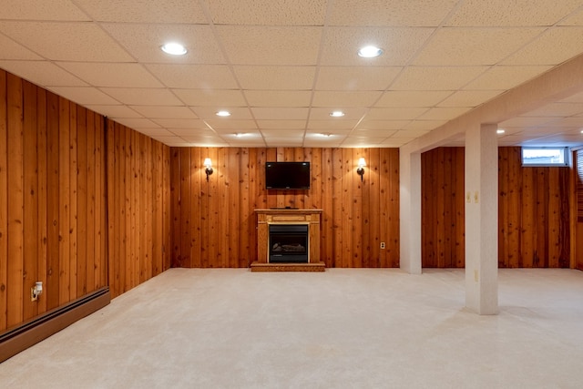 basement with a paneled ceiling, wood walls, carpet floors, and a baseboard heating unit