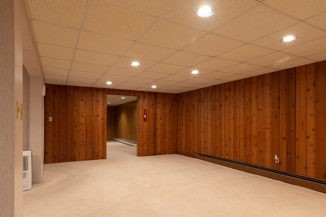 basement featuring carpet flooring, a paneled ceiling, wood walls, and a baseboard heating unit