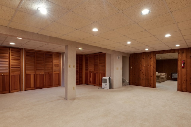 basement featuring carpet flooring, a drop ceiling, and wooden walls