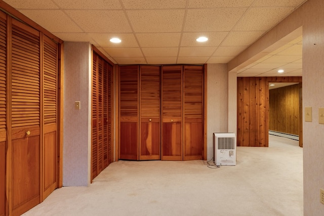 carpeted bedroom with a paneled ceiling, two closets, wood walls, and a baseboard heating unit