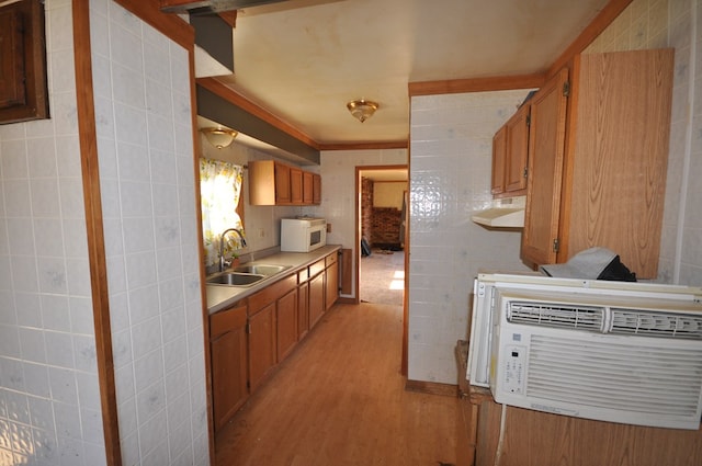 kitchen with light wood-type flooring, sink, and tile walls