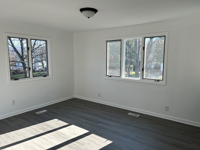 empty room featuring dark wood-type flooring and a healthy amount of sunlight