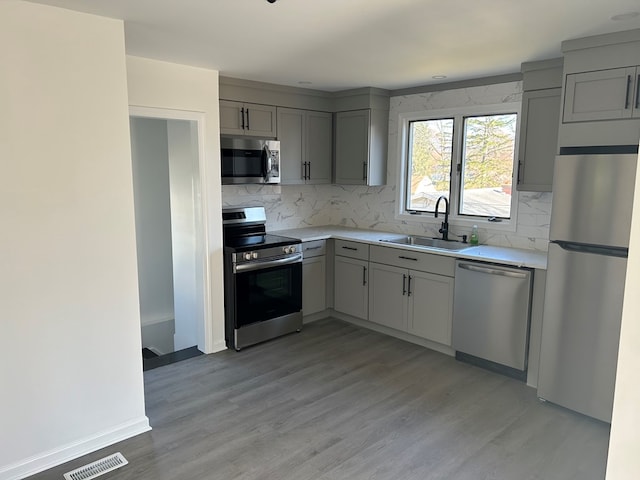 kitchen featuring gray cabinetry, light wood-type flooring, sink, and appliances with stainless steel finishes