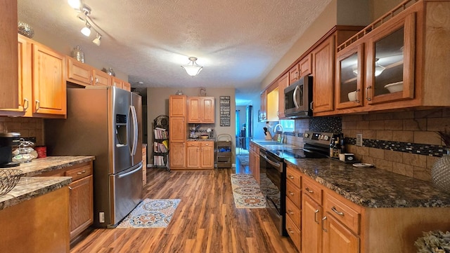 kitchen with dark hardwood / wood-style flooring, backsplash, dark stone countertops, a textured ceiling, and appliances with stainless steel finishes