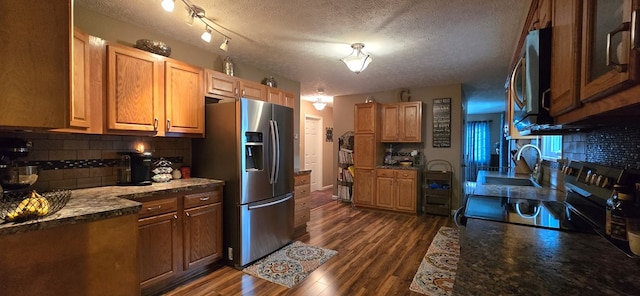 kitchen with sink, dark hardwood / wood-style floors, dark stone countertops, a textured ceiling, and stainless steel appliances